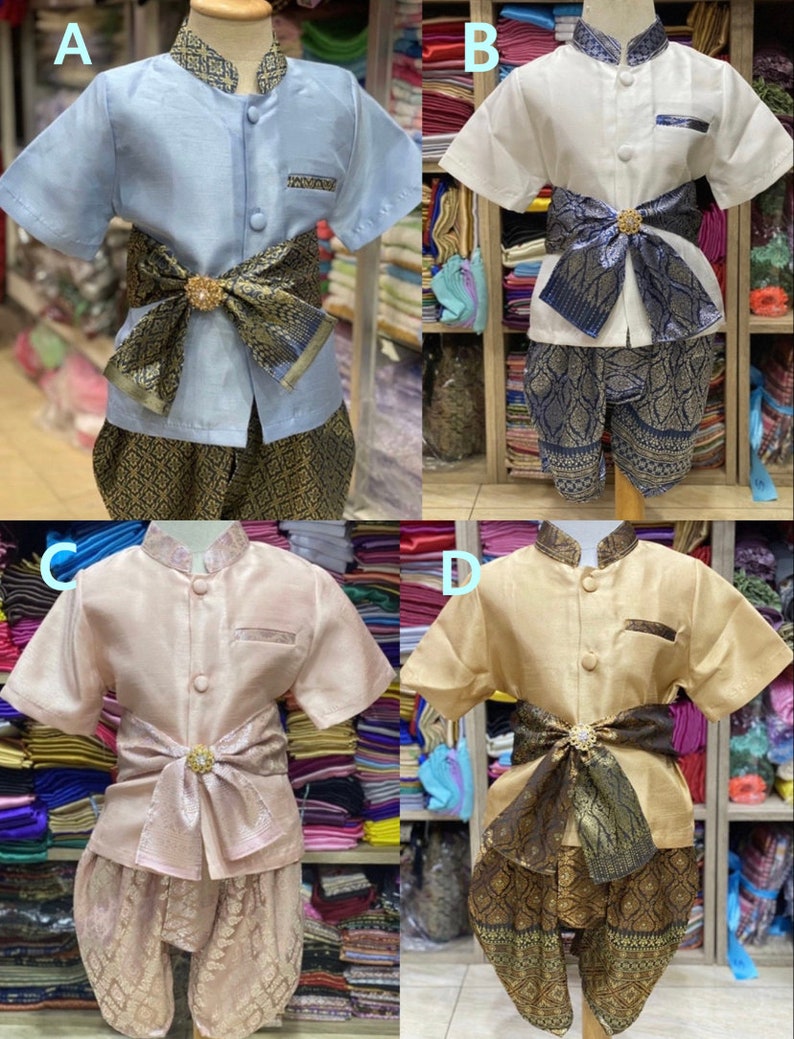 May include: Four traditional Thai children's outfits in various colors: light blue, white, pink, and tan. Each set includes a short-sleeved shirt, patterned pants, and a decorative sash with a central embellishment. The outfits are displayed on mannequins.