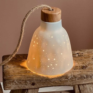 Peut inclure: Un luminaire suspendu en céramique blanche avec un dessus en bois et un cordon en jute. La lumière a un motif en forme d'étoile et est éclairée, projetant une lueur chaude.