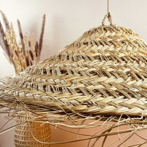 May include: A large, round, woven lampshade made of natural straw with a light brown colour. The lampshade has a unique, slightly conical shape and a textured surface.