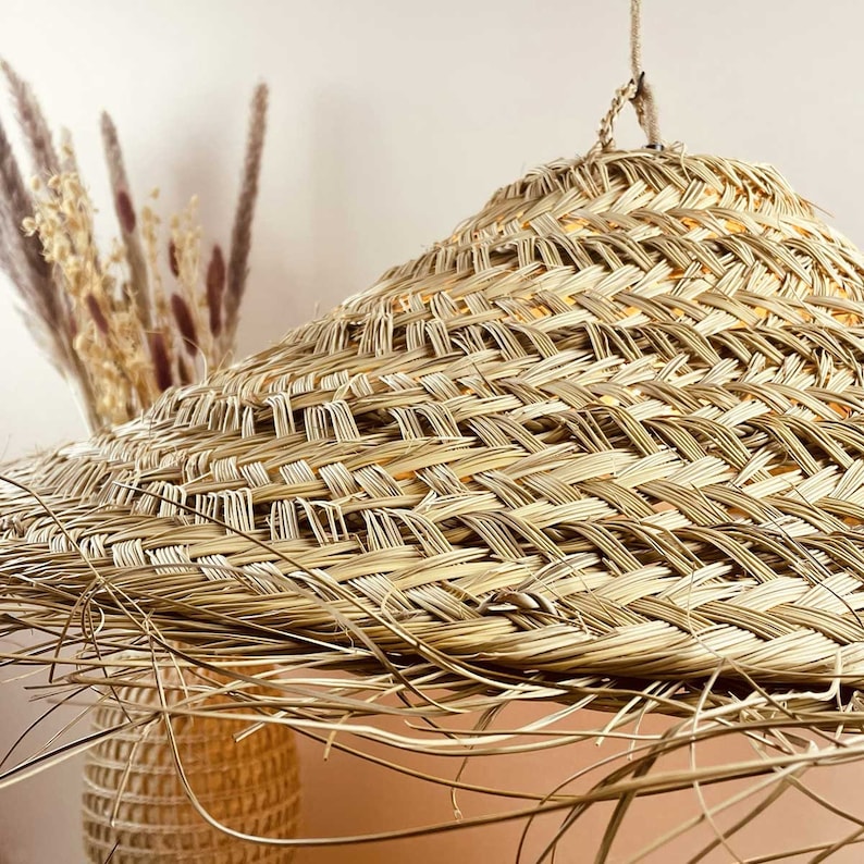 May include: A large, round, woven lampshade made of natural straw with a light brown colour. The lampshade has a unique, slightly conical shape and a textured surface.