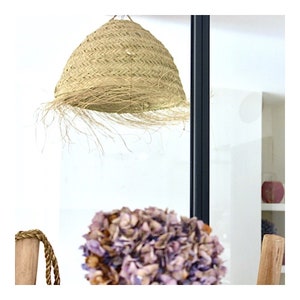 May include: A natural woven straw lampshade with a fringe detail hangs from the ceiling. The lampshade is a light beige color and has a round shape.
