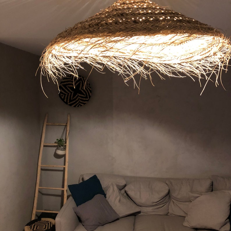 May include: A woven straw lampshade hangs from the ceiling, casting a warm glow on a living room with a sofa and cushions.