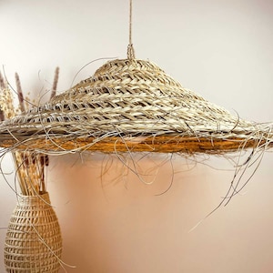 May include: A woven straw lampshade hanging from a cord. The lampshade is a wide, flat disc with a slightly domed top. The straw is woven in a tight, intricate pattern.