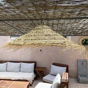 May include: A large, round, woven straw lampshade hangs from a hook. The lampshade is light brown and has a fringe around the bottom edge.