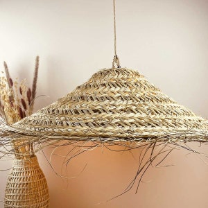 May include: A large, round, woven straw lampshade hangs from a cord. The lampshade is light brown and has a natural, rustic look.