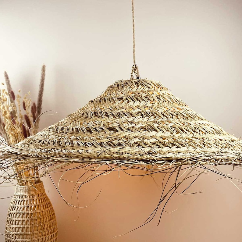 May include: A large, round, woven straw lampshade hangs from a cord. The lampshade is light brown and has a natural, rustic look.