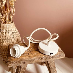 Könnte beinhalten: Eine weiße Deckenleuchte mit einem weißen Kabel und einem weißen Keramiksockel. Die Leuchte steht auf einem Holzhocker.