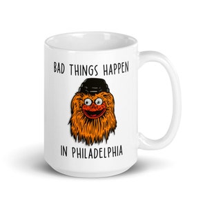 May include: White ceramic mug with a black and orange illustration of the Philadelphia Flyers mascot, Gritty, wearing a hockey helmet. The text "Bad things happen in Philadelphia" is printed on the mug.