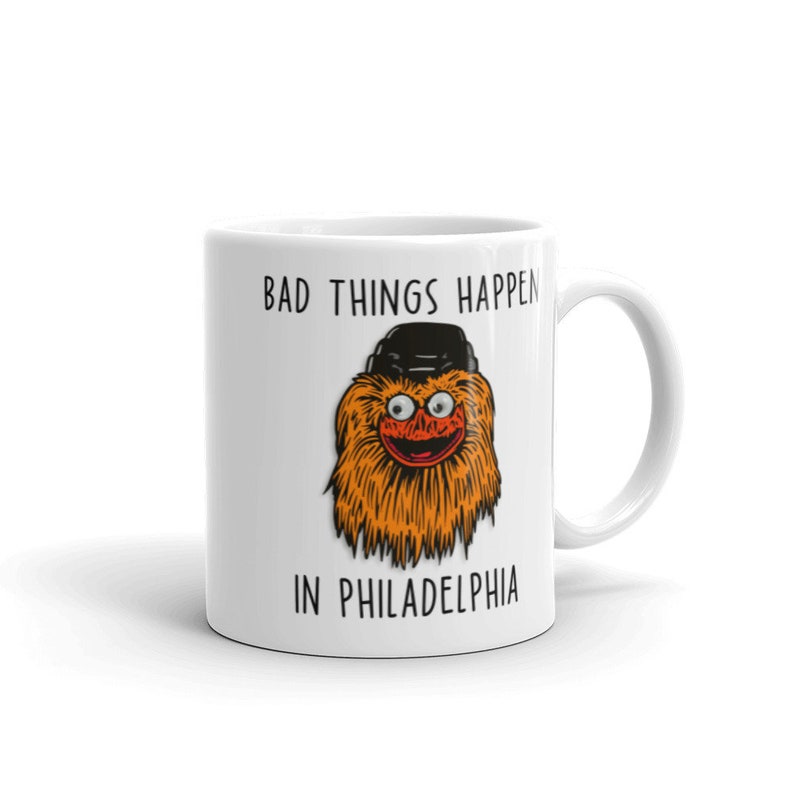 May include: White ceramic coffee mug with a black and orange illustration of the Philadelphia Flyers mascot, Gritty, wearing a black hat. The text "Bad things happen in Philadelphia" is printed on the mug.