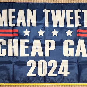 May include: A blue flag with white text that reads "MEAN TWEETS CHEAP GAS 2024". There are two red stripes and four white stars above the text.