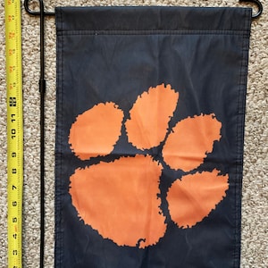 May include: A black garden flag with an orange paw print design. The flag is attached to a black metal pole.