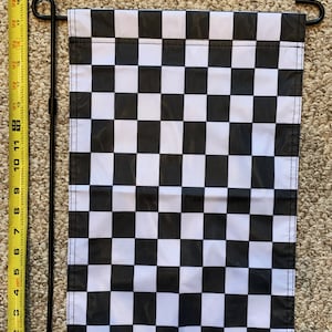 May include: A black and white checkered flag with a metal pole for hanging. The flag is approximately 11 inches wide and 17 inches long.