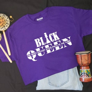 May include: Purple t-shirt with white text that reads "Black Queen" and "The Most Sought After Piece In The Game".