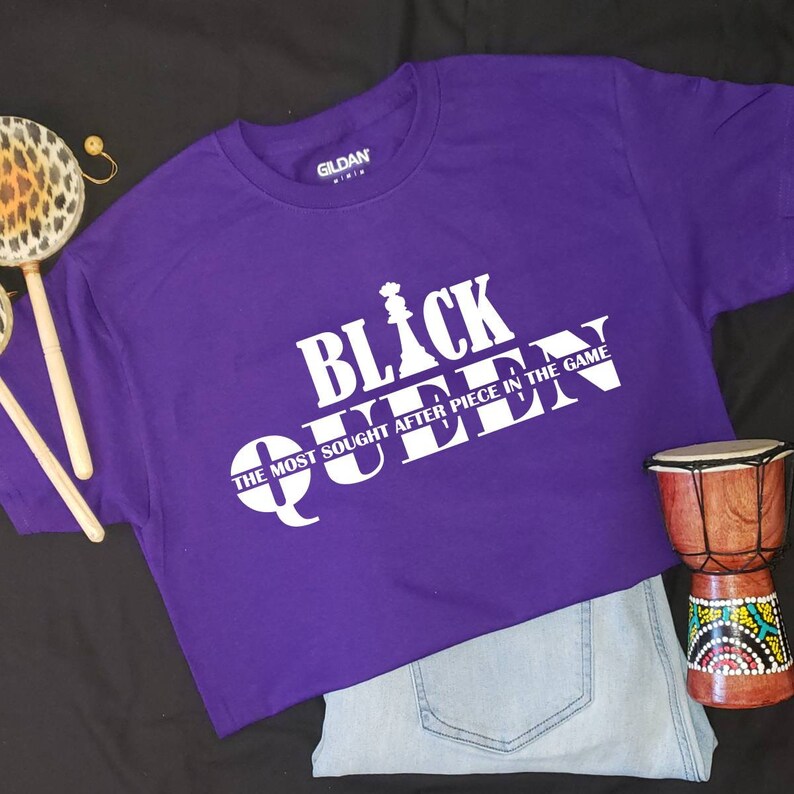 May include: Purple t-shirt with white text that reads "Black Queen" and "The Most Sought After Piece In The Game".