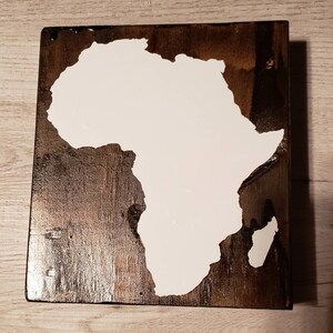 May include: A wooden sign with a white outline of the continent of Africa. The sign has a dark brown wood grain.