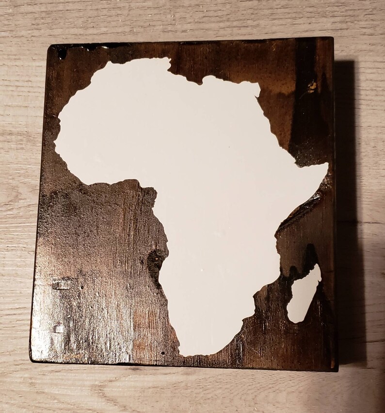 May include: A wooden sign with a white outline of the continent of Africa. The sign has a dark brown wood grain.
