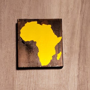 May include: A wooden sign with a yellow painted outline of the continent of Africa.
