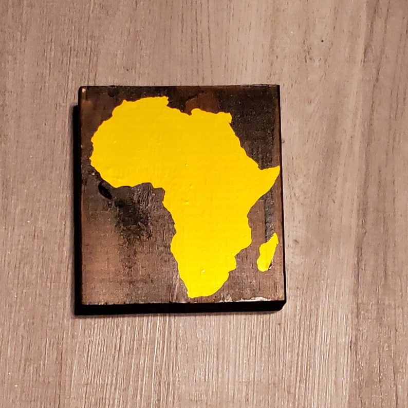 May include: A wooden sign with a yellow painted outline of the continent of Africa.