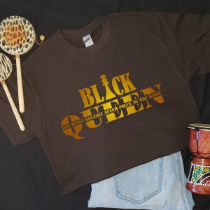 May include: A brown t-shirt with a gold graphic that says "Black Queen" and "The Most Sought After Piece In The Game".