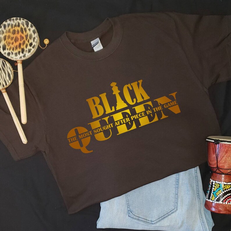 May include: A brown t-shirt with a gold graphic that says "Black Queen" and "The Most Sought After Piece In The Game".