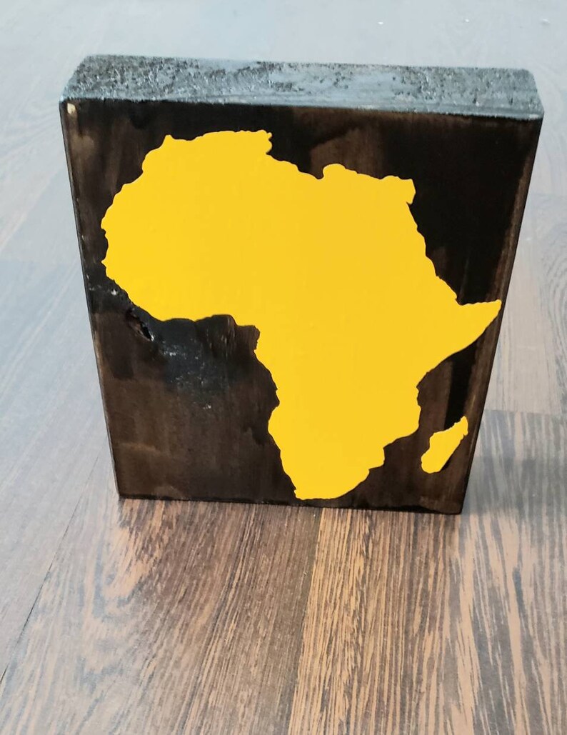 May include: A wooden block with a yellow silhouette of the continent of Africa painted on it. The block is stained dark brown.