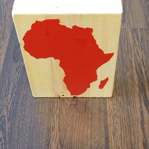 May include: A wooden block with a red painted outline of the continent of Africa.