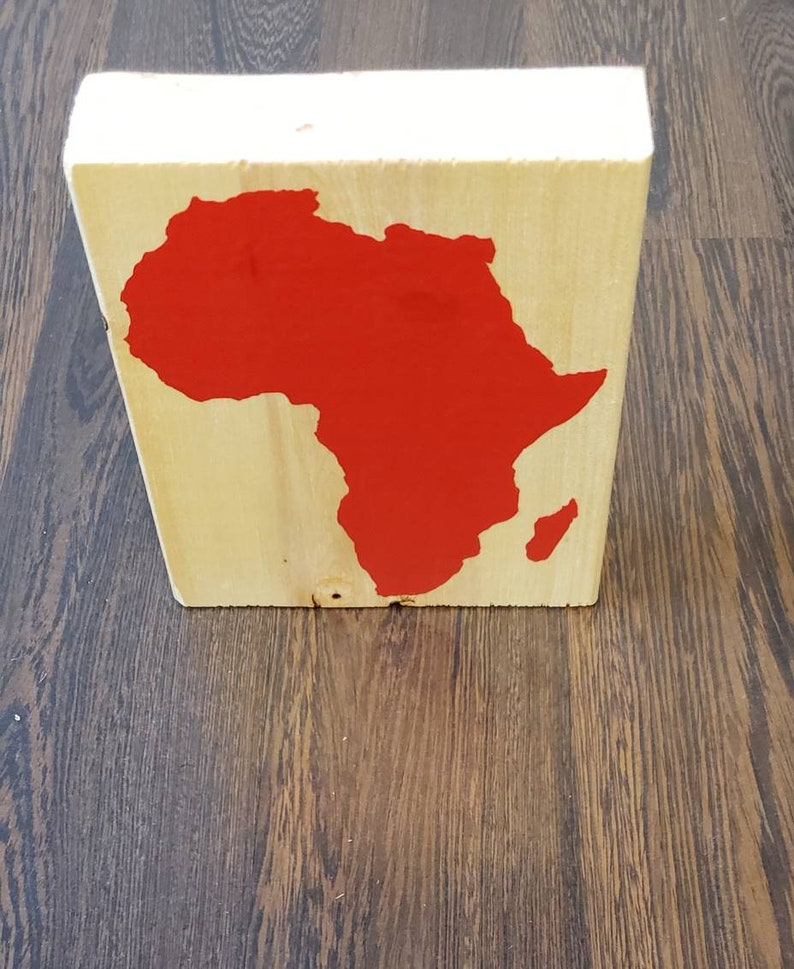May include: A wooden block with a red painted outline of the continent of Africa.