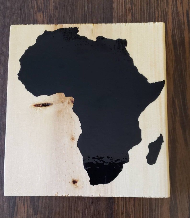 May include: A wooden plaque with a black silhouette of the continent of Africa. The plaque is made of light wood with a natural grain.