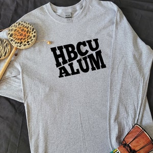 May include: Gray long-sleeve t-shirt with black text that reads "HBCU ALUM" in a diagonal design.