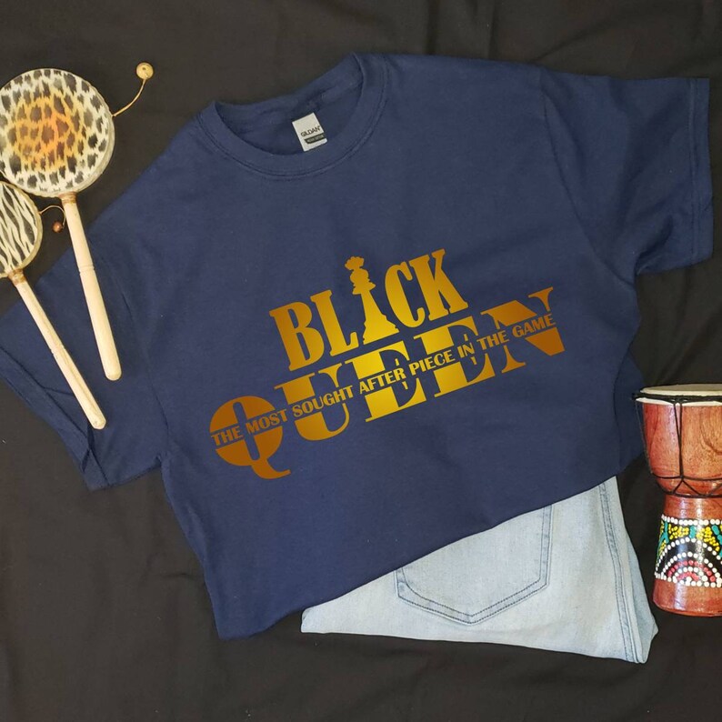 May include: A navy blue t-shirt with a gold graphic that says "Black Queen" and "The Most Sought After Piece In The Game".