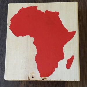 May include: A red painted wooden sign with the outline of the continent of Africa.