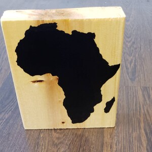 May include: A wooden block with a black silhouette of the continent of Africa painted on it.