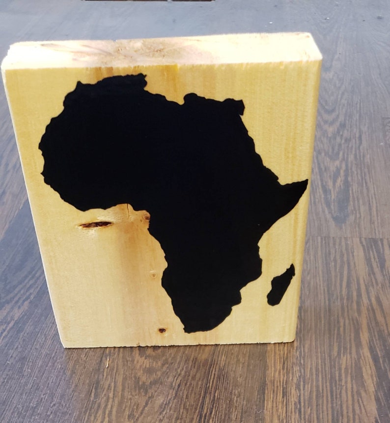 May include: A wooden block with a black silhouette of the continent of Africa painted on it.