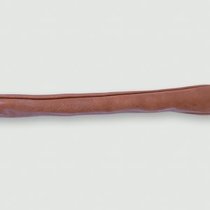 Könnte beinhalten: Eine braune Golfschlägerhaube aus Leder. Die Haube ist lang und röhrenförmig, mit einem abgerundeten Ende und einer gefalteten, genähten Öffnung. Die Haube besteht aus glattem, mattem Leder.