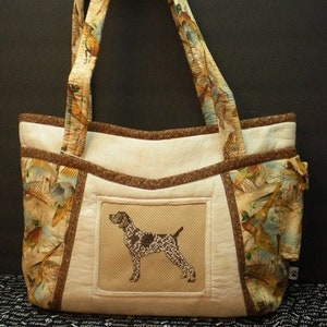 May include: A white fabric tote bag with brown trim and a brown fabric pocket. The bag has a brown and white patterned fabric with birds on it. The pocket has a brown fabric with a white embroidered image of a brown and white dog.