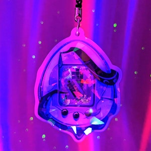 May include: A clear purple and blue iridescent keychain with a glittery design of a Tamagotchi.