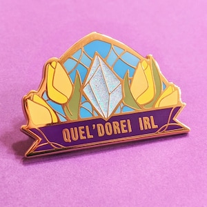 Puede incluir: Un pin de esmalte dorado con un diseño de vitral con flores amarillas, un cristal azul y blanco y el texto "Quel'dorei IRL".