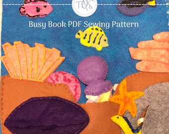 Op de afbeelding: Een vilt pagina van een druk boek met een onderwaterthema. De blauwe achtergrond toont vilten vissen, koraal en een zeester. De tekst "Busy Book PDF Sewing Pattern" is in het wit weergegeven.