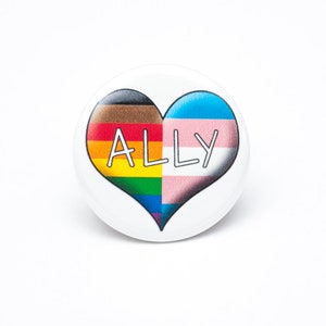 May include: A white button with a heart-shaped design. The heart is divided in half, with the left side showing the progression of the pride flag and the right side showing the transgender pride flag. The word "ALLY" is written in white across the heart.