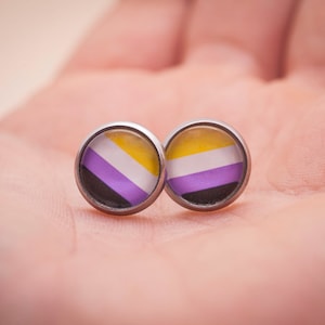 May include: A pair of silver earrings with a yellow, white, purple, and black flag design.