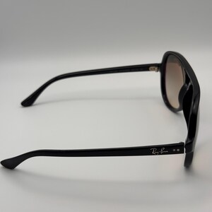 Puede incluir: Gafas de sol negras con lentes degradadas. Las gafas tienen una montura gruesa y el logotipo de Ray-Ban es visible en la patilla. Las lentes hacen una transici&oacute;n de marr&oacute;n claro a un tono m&aacute;s oscuro.