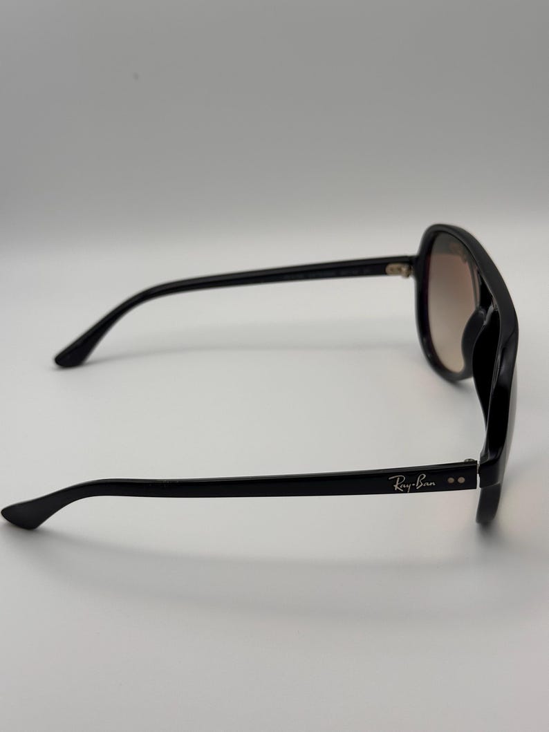 Puede incluir: Gafas de sol negras con lentes degradadas. Las gafas tienen una montura gruesa y el logotipo de Ray-Ban es visible en la patilla. Las lentes hacen una transici&oacute;n de marr&oacute;n claro a un tono m&aacute;s oscuro.