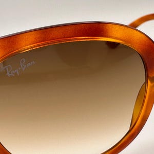 May include: Close-up of Ray-Ban sunglasses with a tortoiseshell frame. The lenses have a gradient tint, transitioning from a darker shade at the top to a lighter shade at the bottom. The Ray-Ban logo is visible on the lens.