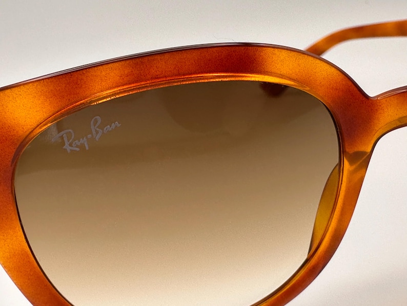 May include: Close-up of Ray-Ban sunglasses with a tortoiseshell frame. The lenses have a gradient tint, transitioning from a darker shade at the top to a lighter shade at the bottom. The Ray-Ban logo is visible on the lens.