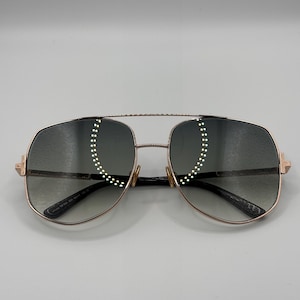 Może przedstawiać: Różowe złote okulary przeciwsłoneczne typu aviator z gradientowymi soczewkami. Okulary mają podwójny mostek i prostokątny kształt. Zauszniki i mostek są w kolorze różowego złota. Soczewki mają szary gradient.