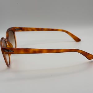 May include: Brown tortoiseshell sunglasses with the Ray-Ban logo on the temple. The sunglasses have a classic design with a rounded frame and gradient lenses. The arms are a matching tortoiseshell pattern. The sunglasses are shown on a white background.