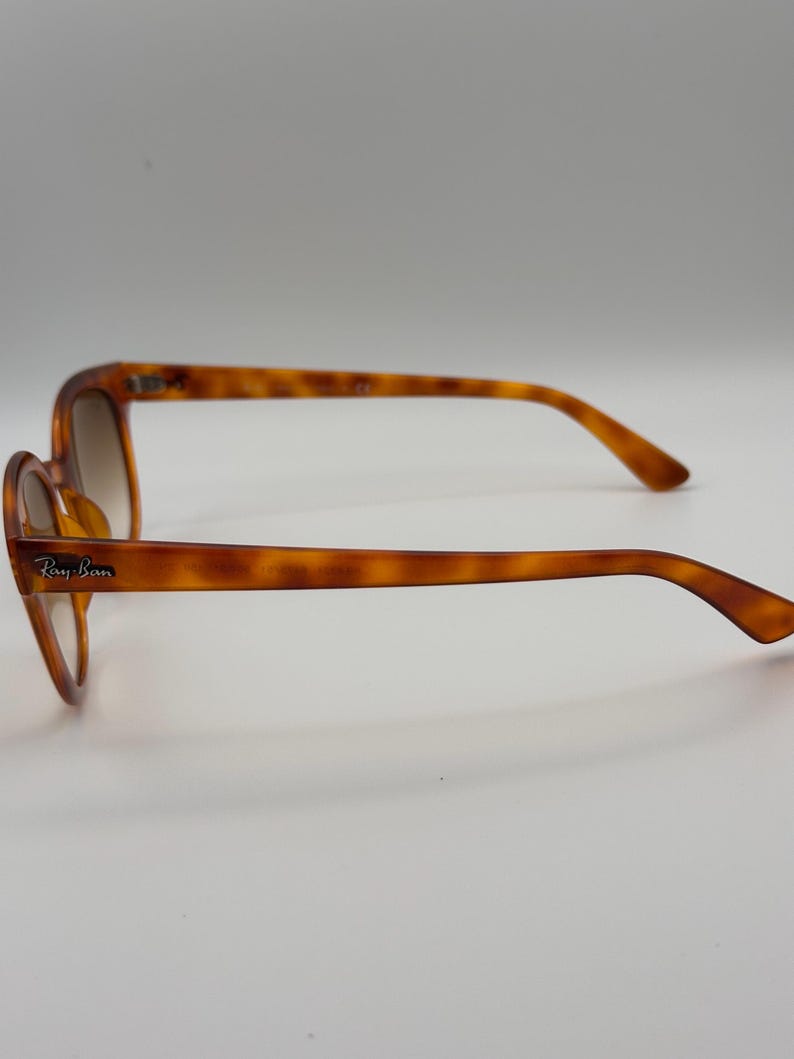 May include: Brown tortoiseshell sunglasses with the Ray-Ban logo on the temple. The sunglasses have a classic design with a rounded frame and gradient lenses. The arms are a matching tortoiseshell pattern. The sunglasses are shown on a white background.