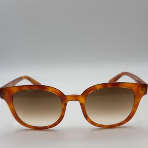 May include: Brown tortoiseshell sunglasses with a rounded frame and gradient lenses. The sunglasses have a classic design and are suitable for everyday wear. The lenses transition from a darker shade at the top to a lighter shade at the bottom.