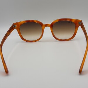 May include: Amber tortoiseshell sunglasses with brown gradient lenses. The frames have a classic round shape. The arms extend outwards, showcasing the full design. The sunglasses are set against a plain white background. The lenses are a brown gradient.