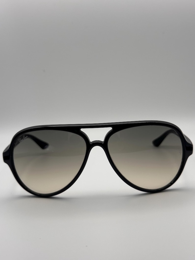 Puede incluir: Gafas de sol aviador negras con lentes degradadas. Las gafas tienen una montura negra gruesa y brillante y una forma cl&aacute;sica de l&aacute;grima. Las lentes pasan de un gris oscuro en la parte superior a un tono m&aacute;s claro en la parte inferior.